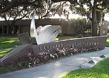 A large sign that says "Lakeland Public Library" with a silver metal sculpture of a swan on top.