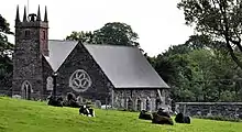 A stone church, with a square tower, and a field of cows in the foreground.