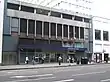 A grey building with blue panels and a dark blue, rectangular sign reading "LANCASTER GATE STATION" in white letters and people in front