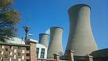 3 enormous waisted vertical concrete cylinders, one emitting a wisp of steam, dwarf a building in the foreground