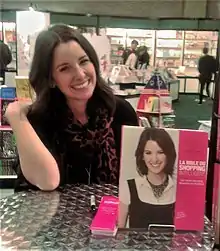 Mme Bareil smiles, while sitting at a table near her book.