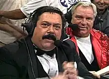 Two men wearing headsets to commentate a professional wrestling event