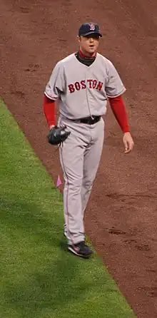 A man in a grey baseball uniform with the word "BOSTON" written across the chest in red letters walks along a baseball field.