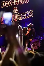 Mars singing to a crowd wearing ablack suit and a fedora hat