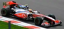 A silver and red Formula One car being driven by a man wearing a yellow crash helmet at speed on a race track