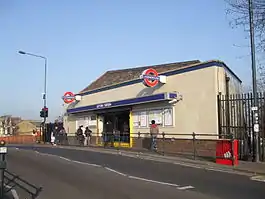 A white-bricked building with a dark blue, rectangular sign reading "LEYTON STATION" in white letters all under a blue sky fading to purple on the horizon