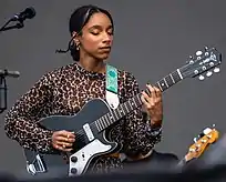 A black woman wearing a leopard print shirt performs with a guitar