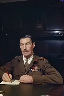 Ronald Scobie poses for a photograph, sitting behind a desk while writing.