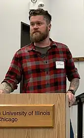 Image 172American man wearing a slim-fitting flannel shirt, a beard, and an undercut, 2019. Sleeve tattoos can be seen. (from 2010s in fashion)