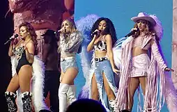 Four young women on a stage before a pink-and-blue backdrop.