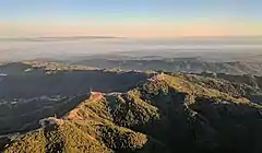 Loma Prieta (the peak just right of center) and other nearby peaks are festooned with television broadcast towers and other communication towers, serving the Santa Clara Valley.  Fog-shrouded Monterey Bay and the Monterey peninsula are visible in the background in this late-afternoon approach to San José International Airport.