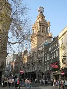 The front of a theatre is viewed from across a street in daytime. There are several entrances. The theatre is surmounted by a globe with the theatre's name running round it.