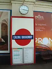 A red framed panel contains a red disc with a slightly wider dark blue band across the centre with the words "EALING BROADWAY".