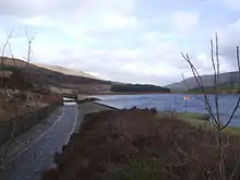 Image 14At the Rhodeswood reservoir dam, we see the outflow canal from the Torside Reservoir dam, alongside the Rhodeswood Reservoir. The Torside dam  can be seen in the distance. To the right is Shining Clough Moss and Bleaklow. To the left Bareholm Moss and Black Hill (from Longdendale Chain)