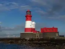 The lighthouse's curved brick foundation supports the stout conical red-and-white-striped tower and adjacent building.