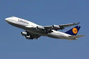 A large white and blue four-engine jet airliner with union tail fin, with landing gear extended