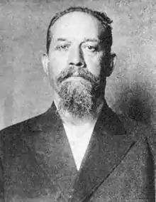 A black-and-white photograph of a man with short hair, moustache, and goatee