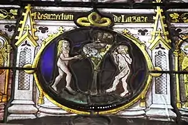 Medieval stained glass medallion depicting the Temptation of Adam and Eve, a man and a woman are naked around a tree bearing fruit and in which there is a snake, the woman is holding an apple and the man has begun to eat another.