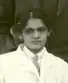 An Indian woman's face; she is wearing a white doctor's coat. Her dark hair is parted center and pinned up.