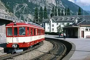 Boxy Red-and-white train on double-track next to platform and single-story building