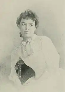 B&W portrait photo of a seated young woman in a reclining position, wearing a white dress.