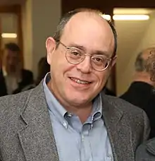 middle-aged, balding white man wearing glasses, shirt, and suit jacket, smiling at camera