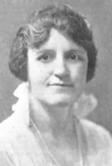 A white woman wearing a white blouse with a high collar