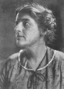 1914 photograph of a middle-aged white woman, looking up and to her right, wearing a print dress with a round collar.