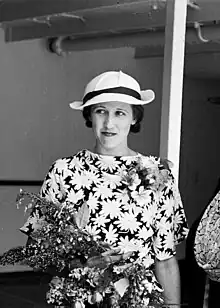 Black-and-white photograph of a woman in a flowered dress holding flowers and wearing a hat