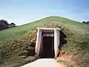 Front view of earth lodge, showing timber doorway into grassy mound