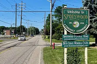 Suburban road with trees; there's a welcome sign in the foreground