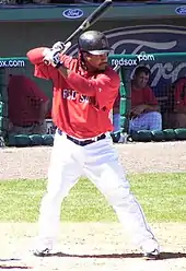 Batter in black hat red top and white pants, batting during spring training for the Red Sox.