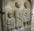 Sandstone bas-relief tombstone of Roman family. There are three figures: a boy, a mother, and a father. They are wearing Roman clothing and hairstyles.