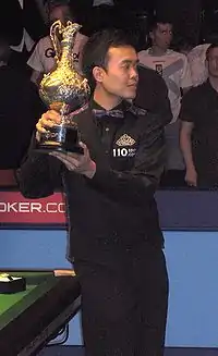 Photograph of Marco Fu standing while holding the Grand Prix trophy