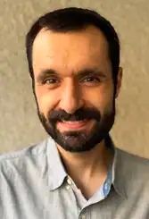 A man with dark hair and a dark beard smiling at the camera.