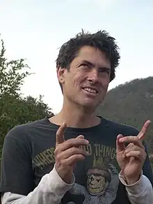 Smiling man outdoors, holding up both index fingers