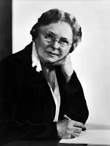 Black and white image of a woman looking at the camera whilst writing.