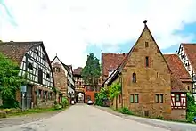 Photograph of the gate (left of center, background) and flanking buildings. The closest, on the right, is the Frühmesserhaus.