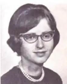 A young white woman with dark hair in a set style, wearing glasses and pearls