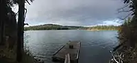 A small lake with the far side visible and the dirt shore in the foreground