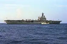 Colour photograph of a grey-painted aircraft carrier at sea. Several white aircraft are parked on its flight deck.