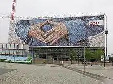 A 2013 CDU billboard near the Berlin Hauptbahnhof uses a mosaic of supporters' photographs to depict the Merkel-Raute.