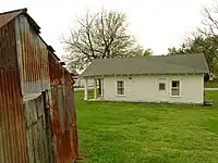 "A white, wooden house with a greenish roof in the middle of a green lawn."