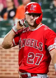 A man in a red baseball jersey and batting helmet with gray pants