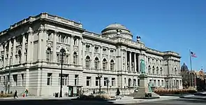 An ornate stone building stretching an entire city block. Architectural features include a dome in the center of the roof, columns along the front of the facade, and two sculpted eagles on the roof.