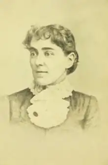 A young white woman with a curled fringe of dark hair, and dark eyebrows, she is wearing a high-collared garment with a kerchief ruffle at her throat