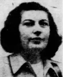 A white woman with dark curly hair, wearing a collared jacket