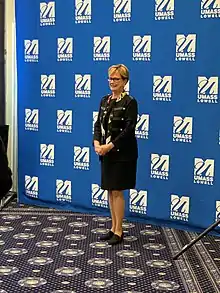 Jacqueline Moloney stands in front of a screen bearing the logo of UMass Lowell.