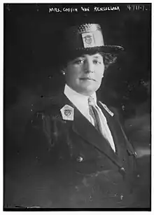 A white woman wearing a dark boater hat and a uniform-style jacket with lapel insignia