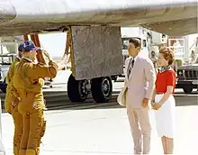 Astronauts salute dignitaries with the Shuttle's rear landing gear and gear door prominently behind, and other landing support vehicles around the orbiter.